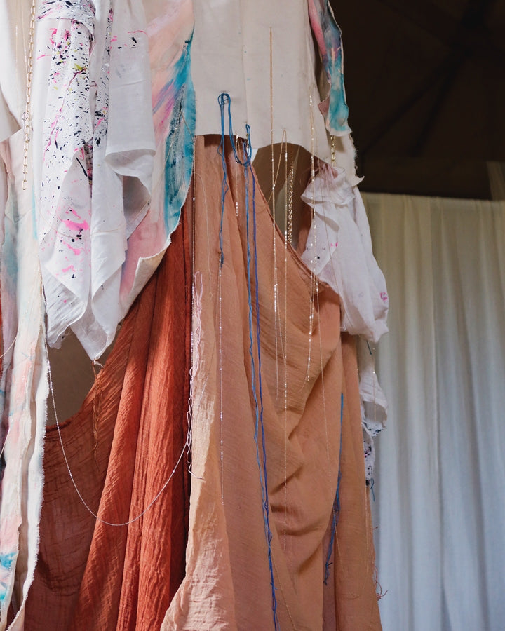 A close up picture of an art installation of draped fabric, embellished with paint, feathers and delicate gold chains.